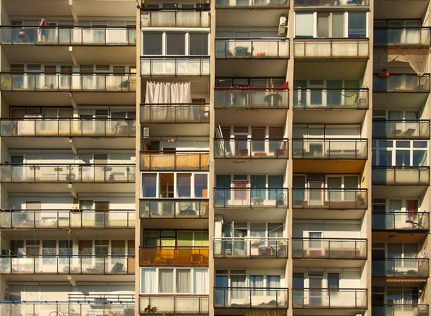 Man stands on a balcony of a concrete apartment building.